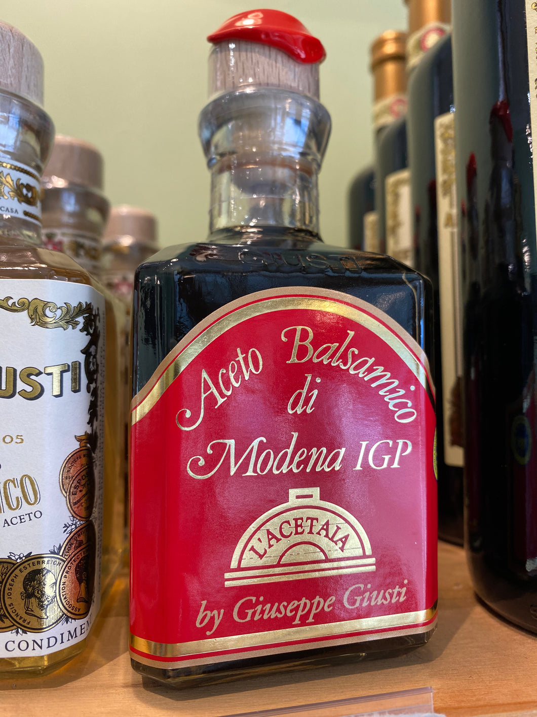 A glass bottle of Giuseppe Giusti Red Label Balsamic Vinegar with wooden stopper and red wax seal on the shop shelf.