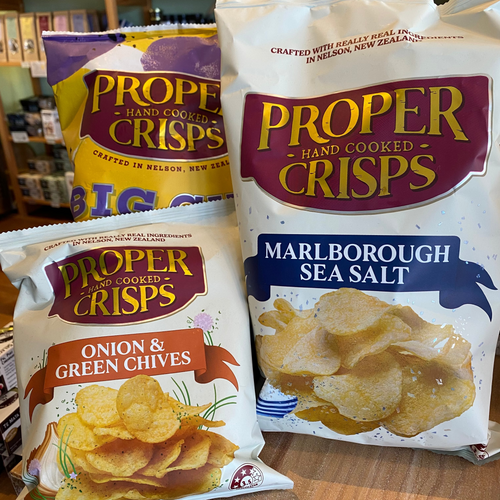 Three bags of Proper Crisps with different flavors on a wooden surface.